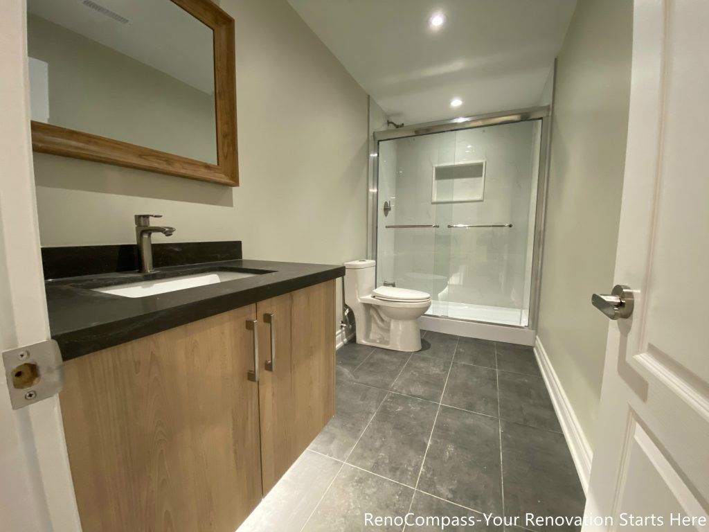 This Aurora basement bathroom renovation was designed to deliver a clean, modern, and highly functional layout within a compact footprint. The space features a wood-tone vanity paired with a dark stone countertop, offering practical storage while adding warmth to the neutral palette. Large-format floor tiles enhance durability and ease of maintenance, while a frameless glass shower enclosure improves openness and light flow throughout the bathroom. Simple, contemporary fixtures and a well-balanced layout ensure everyday comfort and long-term usability, making this basement bathroom suitable for guest use or rental purposes.
City: Aurora
Toronto Contractor: Reno Compass