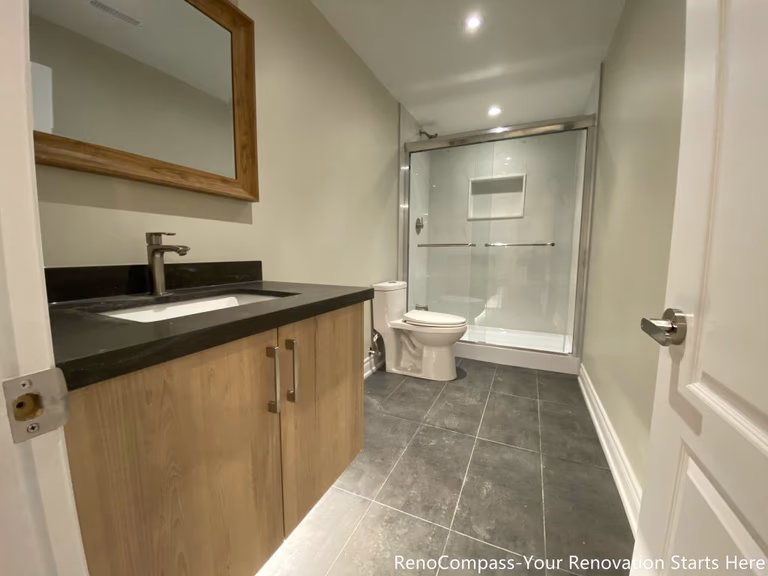 This Aurora basement bathroom renovation was designed to deliver a clean, modern, and highly functional layout within a compact footprint. The space features a wood-tone vanity paired with a dark stone countertop, offering practical storage while adding warmth to the neutral palette. Large-format floor tiles enhance durability and ease of maintenance, while a frameless glass shower enclosure improves openness and light flow throughout the bathroom. Simple, contemporary fixtures and a well-balanced layout ensure everyday comfort and long-term usability, making this basement bathroom suitable for guest use or rental purposes.
City: Aurora
Toronto Contractor: Reno Compass