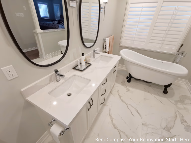he bathroom renovation features elegant marble flooring, which adds visual depth while enhancing durability and ease of maintenance. A custom double vanity provides ample storage and shared functionality, making the space ideal for daily routines without congestion. An independent freestanding bathtub serves as a focal point of the room, offering a spa-inspired experience while maintaining a clean, balanced layout.