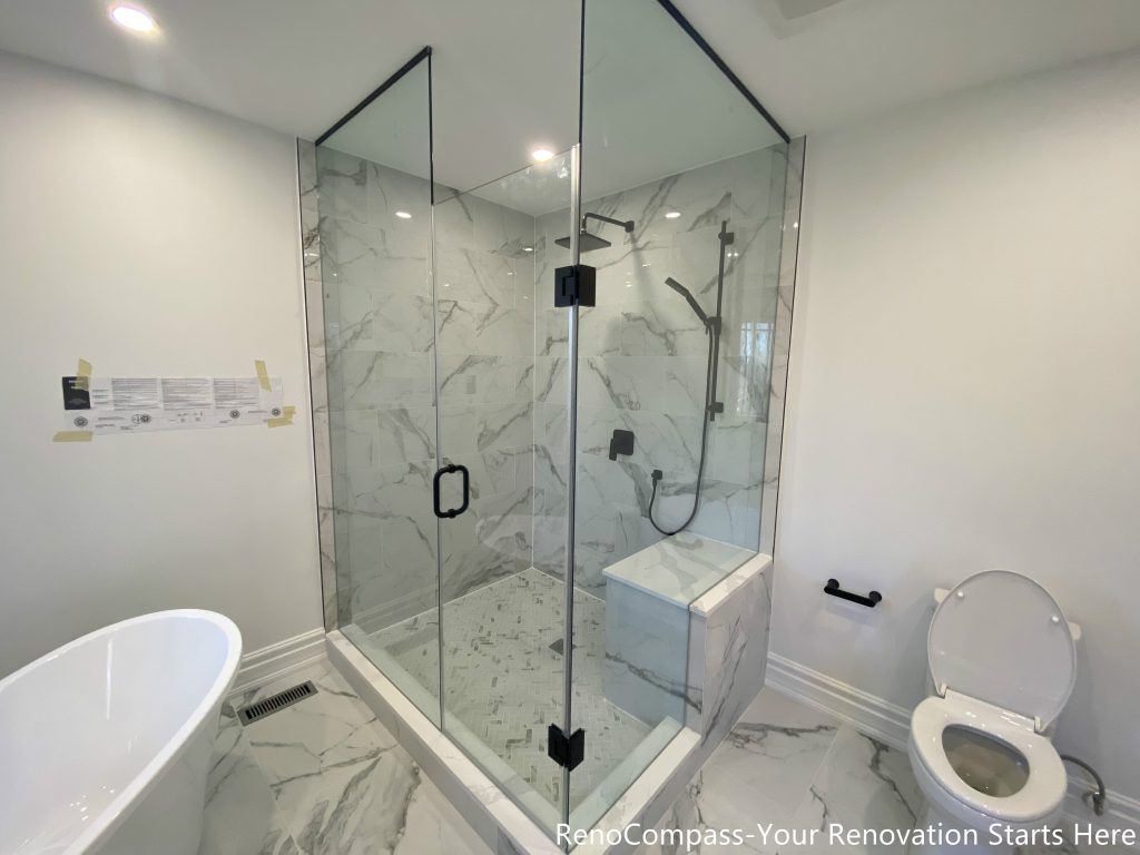 This Thornhill bathroom renovation highlights a spacious frameless glass shower enclosure with a built-in bench, combining comfort and modern functionality. Marble-look porcelain tiles are used throughout the floor and shower walls, creating a cohesive and elegant visual flow. Matte black fixtures add contrast against the light stone surfaces, while the transparent glass panels enhance natural light distribution and spatial openness, resulting in a clean, practical bathroom designed for long-term daily use.