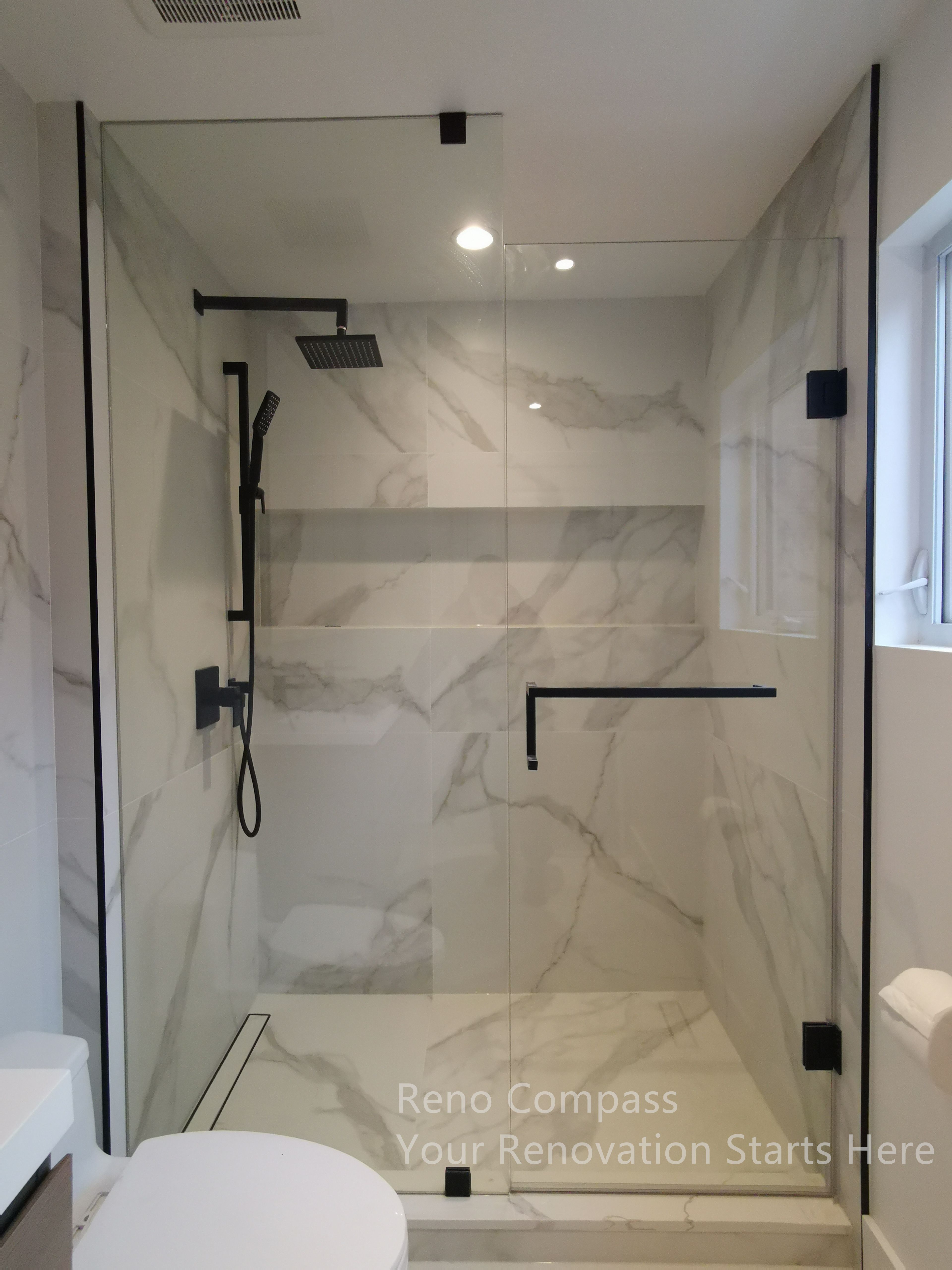 This image showcases the completed shower area as part of a Markham interior renovation. The frameless glass enclosure enhances openness while allowing light to flow throughout the bathroom. Marble-look wall tiles paired with matte black fixtures create a clean, modern contrast, while the integrated niche and walk-in layout improve daily usability and ease of maintenance.