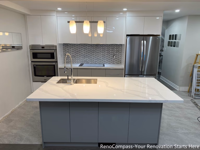 This Mississauga kitchen renovation showcases a modern open-concept design featuring a large quartz island with double sink, custom flat-panel cabinetry, and stainless steel appliances. The upgraded space includes built-in oven units, contemporary backsplash design, and pendant lighting that enhances both functionality and visual appeal. Completed by a trusted Toronto renovation company, this interior renovation focuses on maximizing storage, improving workflow, and creating a bright, elegant kitchen environment ideal for everyday living and entertaining.