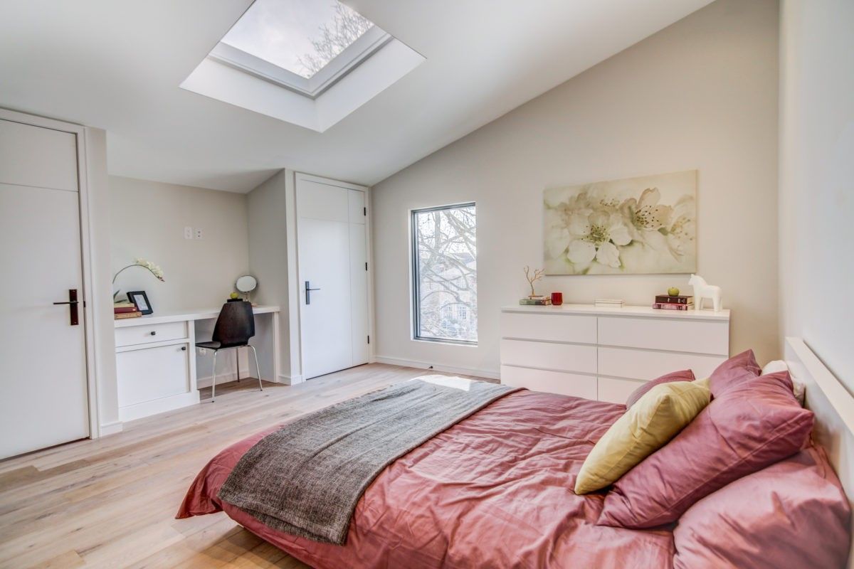 Bright modern bedroom renovation in Toronto featuring a skylight ceiling window, light wood flooring, and custom built-in storage with workspace. Neutral wall tones and large windows create a calm and airy atmosphere, while contemporary furnishings add warmth and comfort. Designed and completed by a professional Toronto renovation company, this bedroom showcases functional layout and elegant modern living.