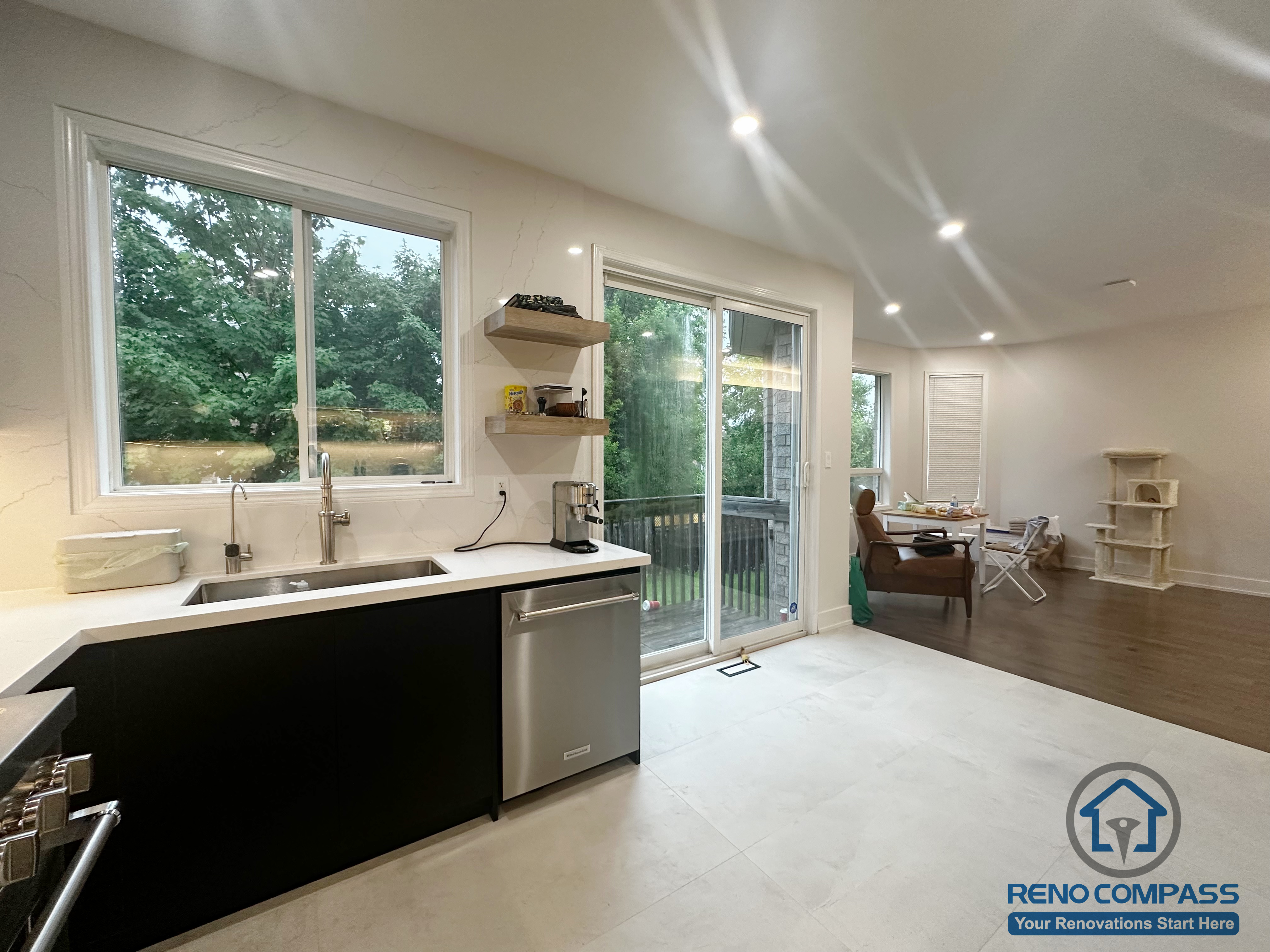 This Oakville interior renovation showcases an open-concept kitchen seamlessly connected to the living area. The design features black lower cabinetry, white countertops, and stainless steel appliances, paired with large windows and sliding glass doors that bring in abundant natural light. Recessed ceiling lighting and clean sightlines enhance the sense of openness, creating a functional and comfortable space that supports both daily living and casual entertaining.