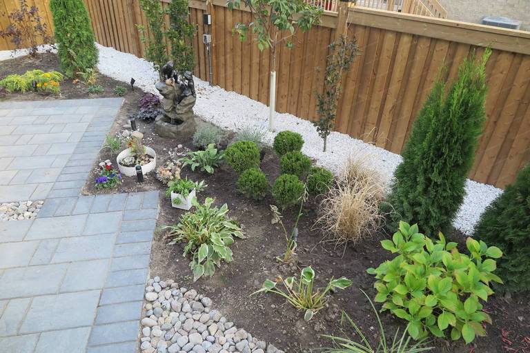 Backyard landscaping renovation in Vaughan featuring a modern interlocking patio, decorative river rock accents, layered garden beds, and a small ornamental water feature. This outdoor design blends hardscape and soft scape elements to create a relaxing backyard environment with strong visual balance and natural landscape texture.