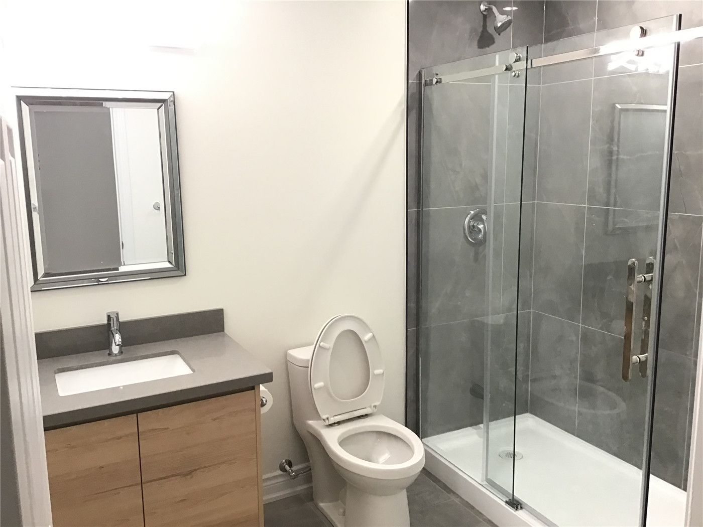 This Aurora basement renovation features a modern bathroom with a sleek glass-enclosed shower, large-format grey tiles, and a contemporary vanity with integrated sink. The clean design maximizes space efficiency while delivering a stylish and functional layout, ideal for a finished basement upgrade.
