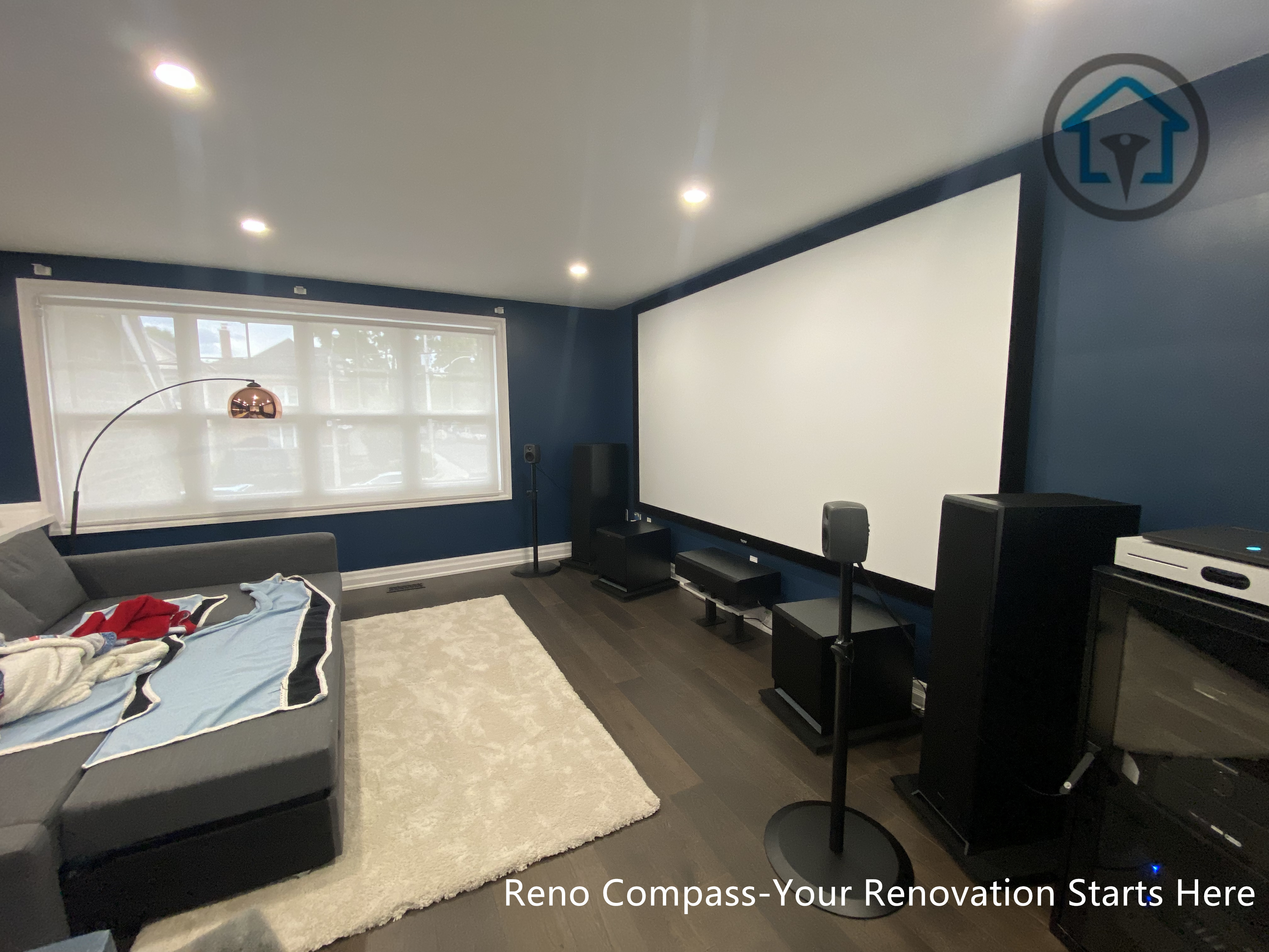 This image highlights a dedicated home theater space completed as part of a residential interior renovation in Toronto. The room is designed with a clear media-focused layout, featuring a full projection screen, integrated speaker system, and controlled lighting for an immersive viewing experience. Dark wall tones reduce glare and enhance screen contrast, while recessed ceiling lights provide balanced ambient illumination. The seating arrangement and circulation were carefully planned to maintain comfort, acoustics, and visual clarity, creating a functional yet refined entertainment environment suited for everyday family use.