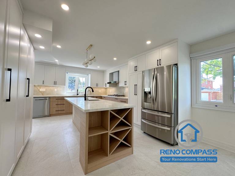A modern kitchen featuring a custom quartz waterfall island with built-in wine storage, floor-to-ceiling cabinetry, stainless steel appliances, and an open-concept layout. Completed as part of a luxury whole home renovation in Markham, Ontario, this contemporary kitchen combines elegant design, functional storage, and premium craftsmanship by Reno Compass.