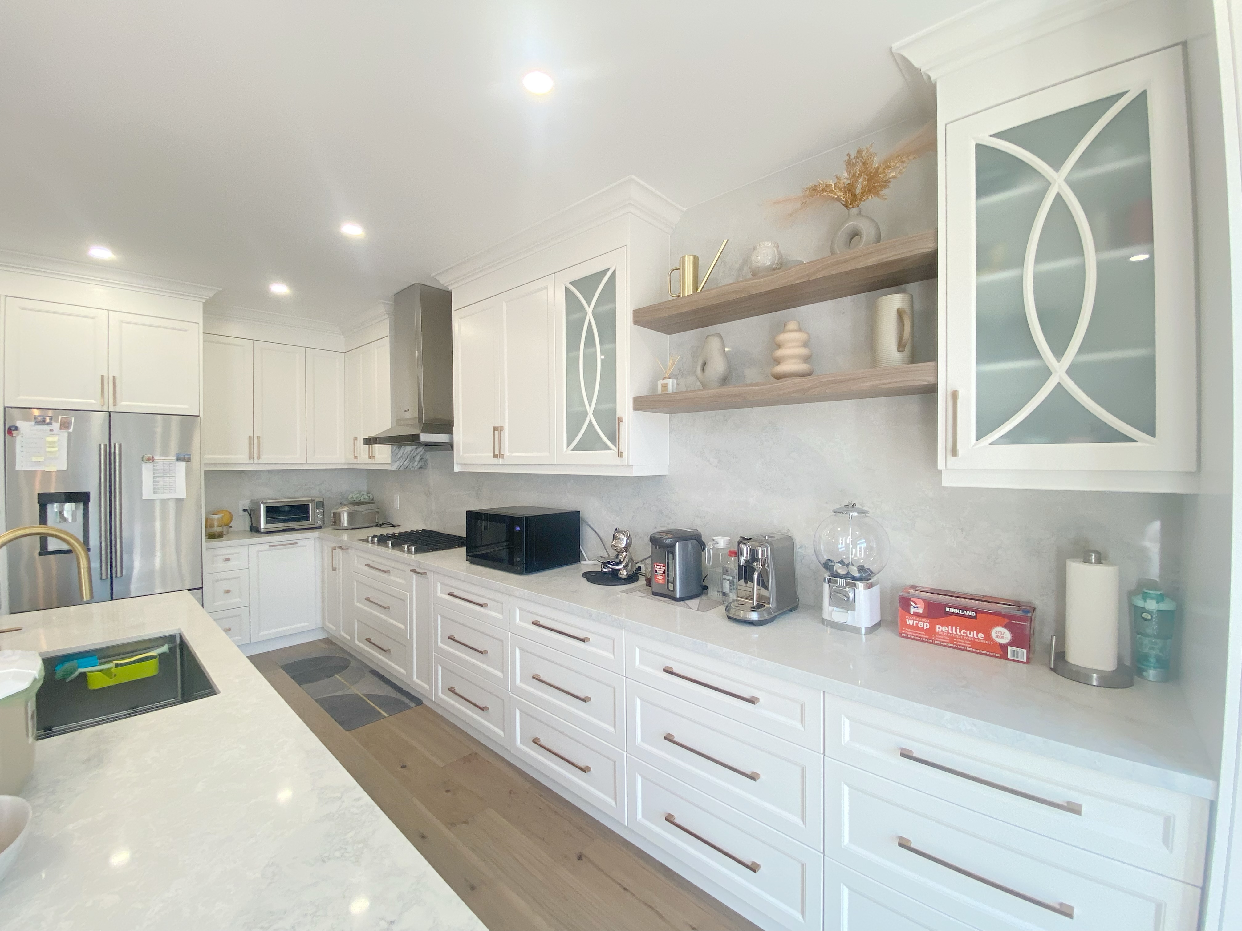 A refined kitchen storage and display wall completed as part of a Richmond Hill interior renovation. This kitchen renovation features custom cabinetry with decorative glass inserts, open wood shelving for everyday items, quartz countertops, and integrated appliance placement for a clean and organized look.
