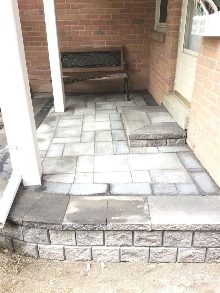 This Oakville interlocking project highlights a well-crafted front porch patio featuring clean grey pavers, a raised stone edge, and a defined step leading to the entrance. The structured layout enhances both aesthetics and usability, creating a welcoming and durable outdoor space. Designed to complement the home’s brick exterior, this interlocking installation adds value, safety, and long-term performance.