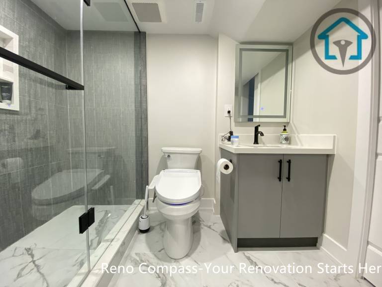 This Stouffville basement bathroom renovation features a walk-in glass shower with large-format tile, a modern vanity with quartz countertop, matte black fixtures, and marble-look floor tiles. Designed for durability and daily comfort, this clean and functional basement bathroom was completed by Reno Compass Inc.