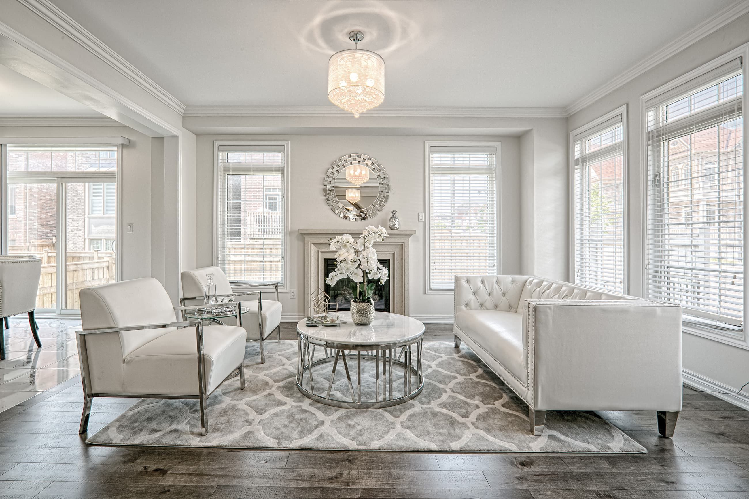 This Toronto modern luxury living room renovation showcases a bright and elegant interior with large windows, premium hardwood flooring, and sophisticated modern classic furnishings. The open layout highlights a custom fireplace feature wall, refined ceiling details, and high-end lighting that enhances the overall atmosphere. Completed by a professional Toronto renovation company, this residential interior project reflects timeless design, functional comfort, and upscale craftsmanship tailored for contemporary living.