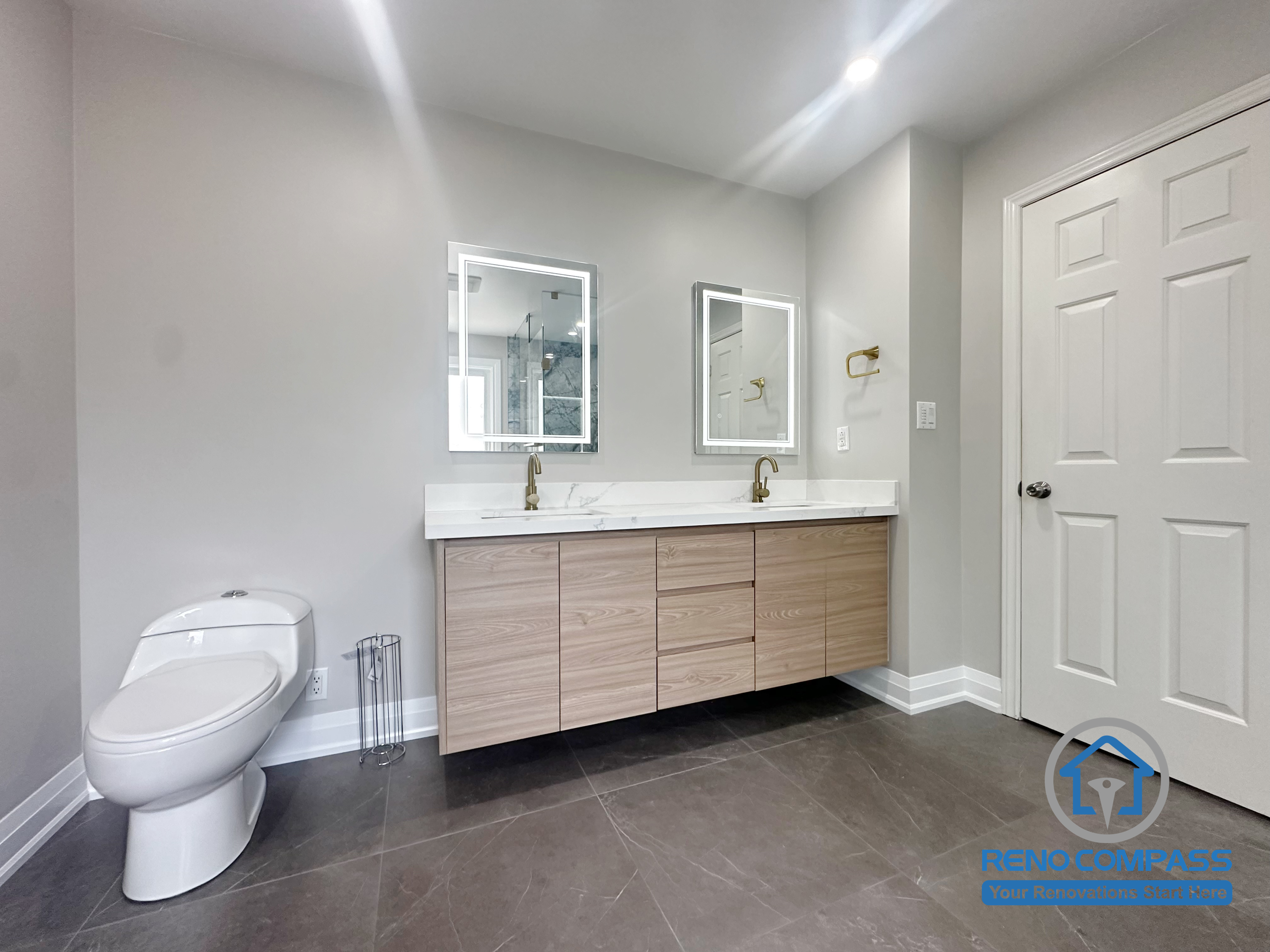 This Oakville bathroom renovation features a streamlined double vanity with integrated wood cabinetry, clean-lined countertops, and backlit mirrors for even task lighting. The design emphasizes practical storage, comfortable daily use, and visual balance, creating a calm and uncluttered bathroom environment. Completed by Reno Compass, this vanity layout reflects a thoughtful approach to modern Oakville bathroom design.