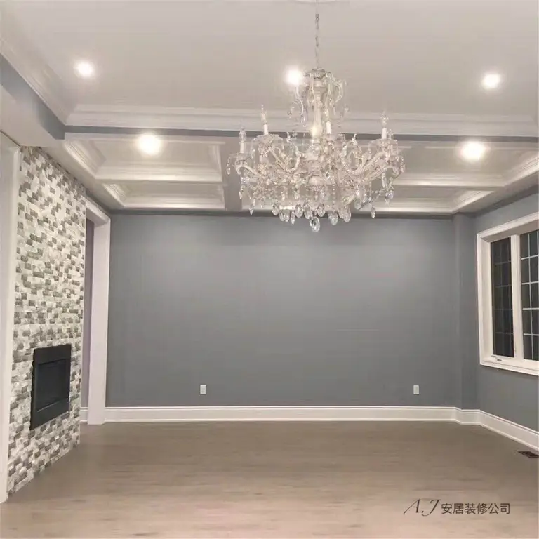 This Scarborough interior renovation showcases a refined living room transformation featuring elegant crown molding, recessed ceiling lighting, and a statement crystal chandelier. The space is enhanced with a modern textured stone fireplace feature wall and neutral grey tones that create a sophisticated, balanced atmosphere. New flooring and clean architectural details complete the design, delivering a bright and contemporary interior upgrade for this Scarborough home.