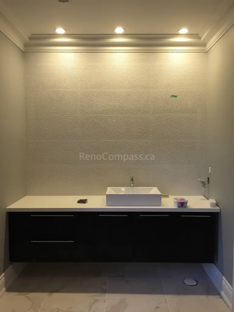 This Toronto interior renovation highlights a modern bathroom vanity upgrade featuring a sleek floating cabinet, contemporary vessel sink, textured feature wall tiles, and elegant recessed lighting. The clean layout and premium finishes create a bright, sophisticated space that blends functionality with modern aesthetics. Completed by Reno Compass Inc., a trusted Toronto renovation company specializing in custom bathroom and interior renovations.