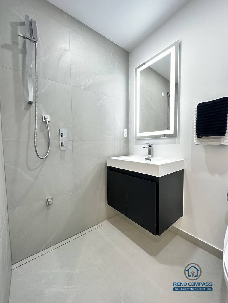 This image features a clean and modern accessible bathroom layout in Brampton, highlighting a floating vanity, integrated LED mirror, and a compact toilet designed for efficient space use. The wall-mounted vanity improves floor clearance, making the bathroom easier to clean and more accessible for daily use and pet care. Neutral-toned tiles and minimal fixtures create a calm, functional environment suitable for barrier-free living. This thoughtfully planned bathroom renovation was completed by an experienced Toronto Renovation Company specializing in accessible and pet-friendly home solutions.