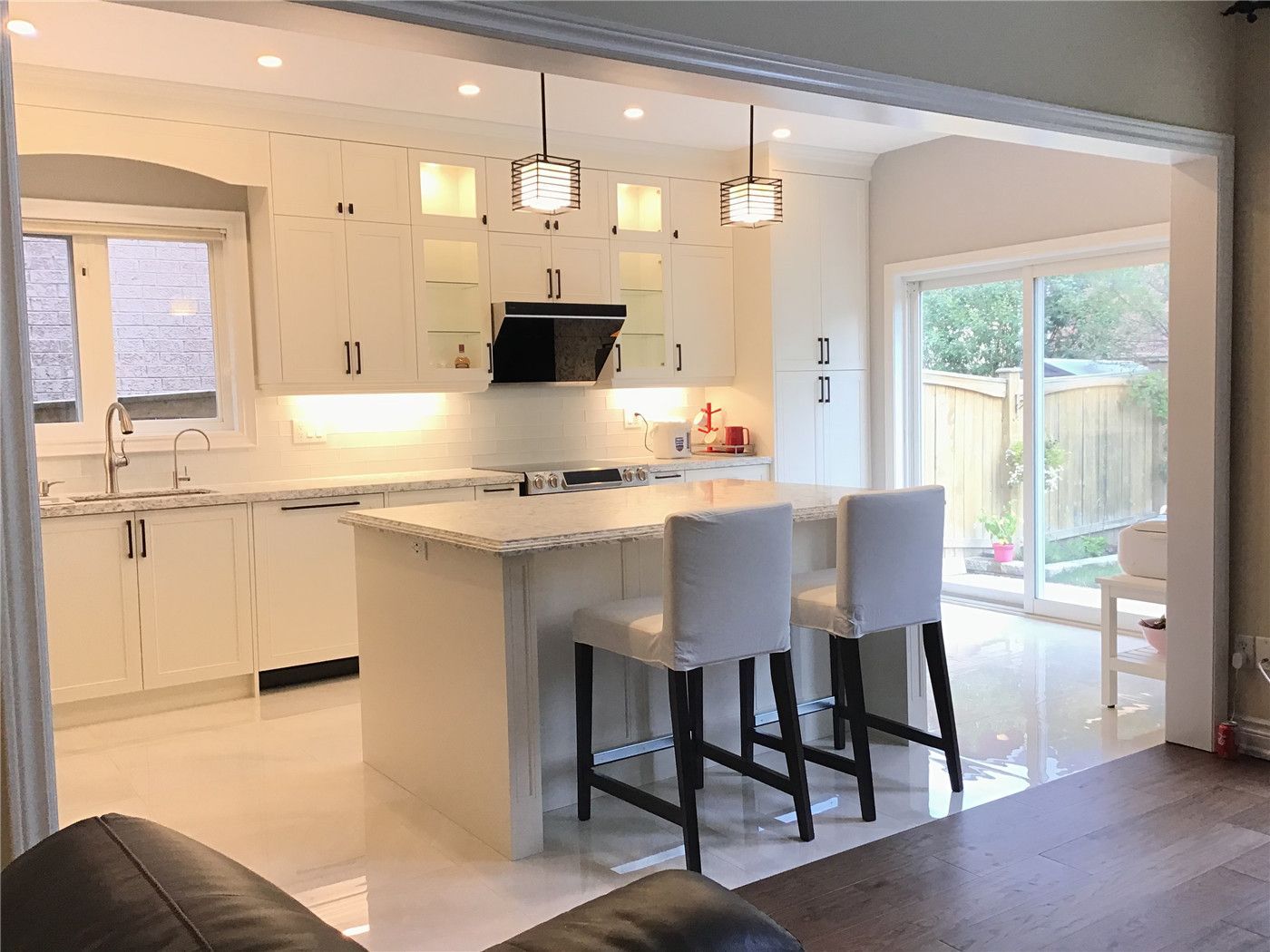This Richmond Hill interior renovation features a bright open-concept kitchen centered around a large quartz island with seating. The space is designed with full-height custom cabinetry, clean white finishes, and modern pendant lighting that enhances both functionality and visual appeal. The symmetrical layout, under-cabinet lighting, and efficient workflow create a welcoming and practical environment for everyday living. Completed by a professional Toronto renovation company, this project reflects a refined and timeless kitchen design.