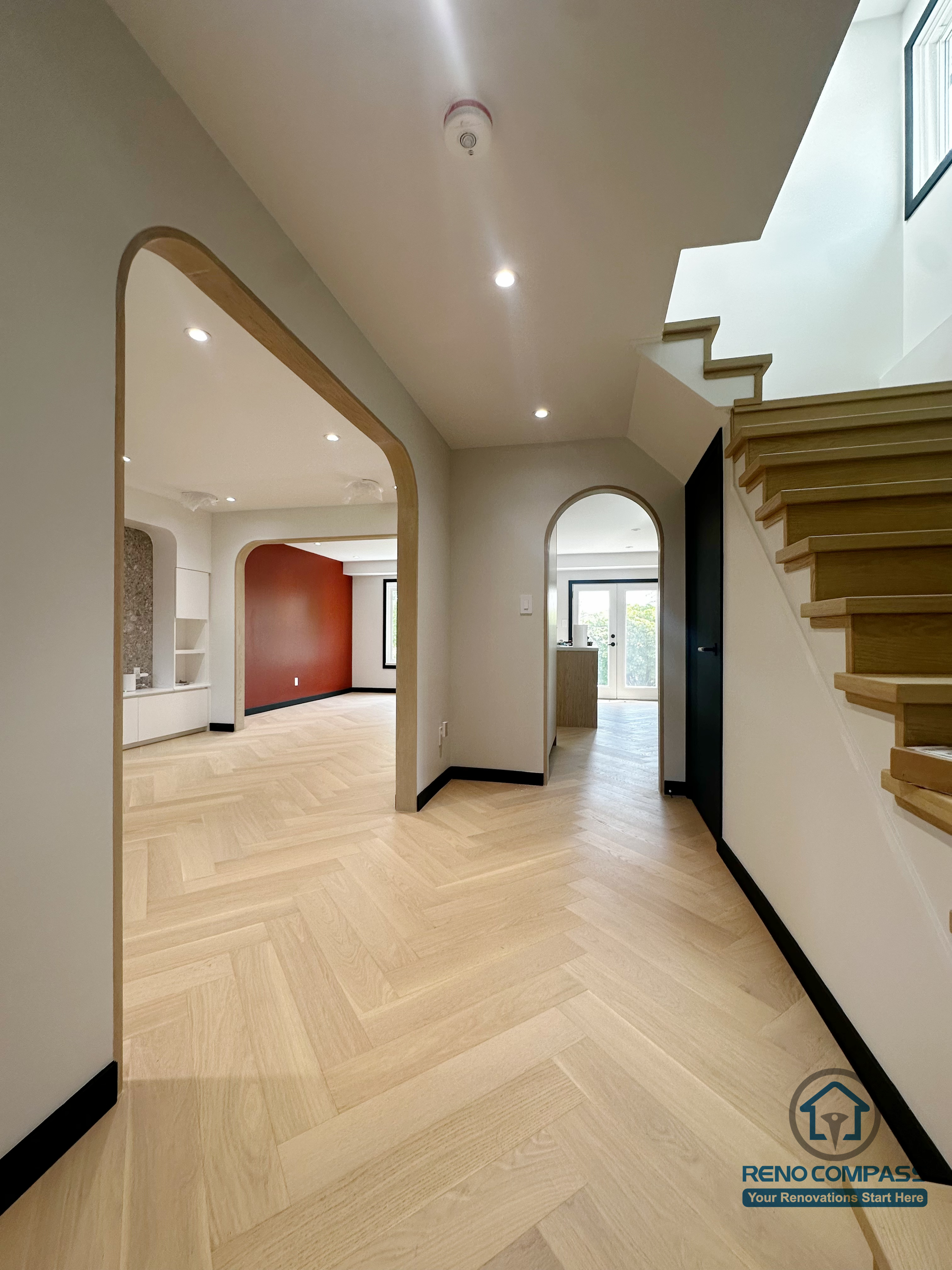 This photo showcases the foyer and staircase area from the Richmond Hill renovation project.
The light herringbone flooring visually enlarges the space, while the black baseboards and soft archway openings create a modern yet welcoming design tone.
The hallway seamlessly connects to the living and kitchen areas, enhancing the flow and cohesion of the entire home.