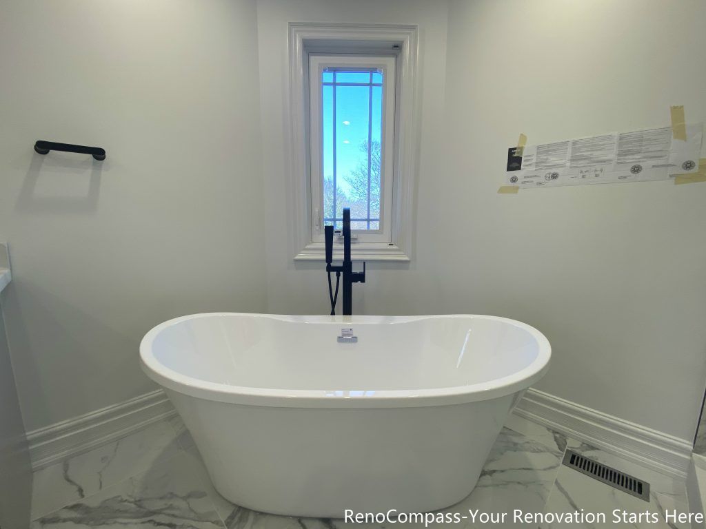 This Thornhill bathroom renovation features a freestanding bathtub positioned beneath a window, creating a calm and balanced focal point within the space. The tub is paired with a matte black floor-mounted faucet, adding a modern contrast to the light marble-look floor tiles. Natural daylight enhances the clean, minimal design, while the open layout promotes comfort, relaxation, and long-term functionality for everyday use.