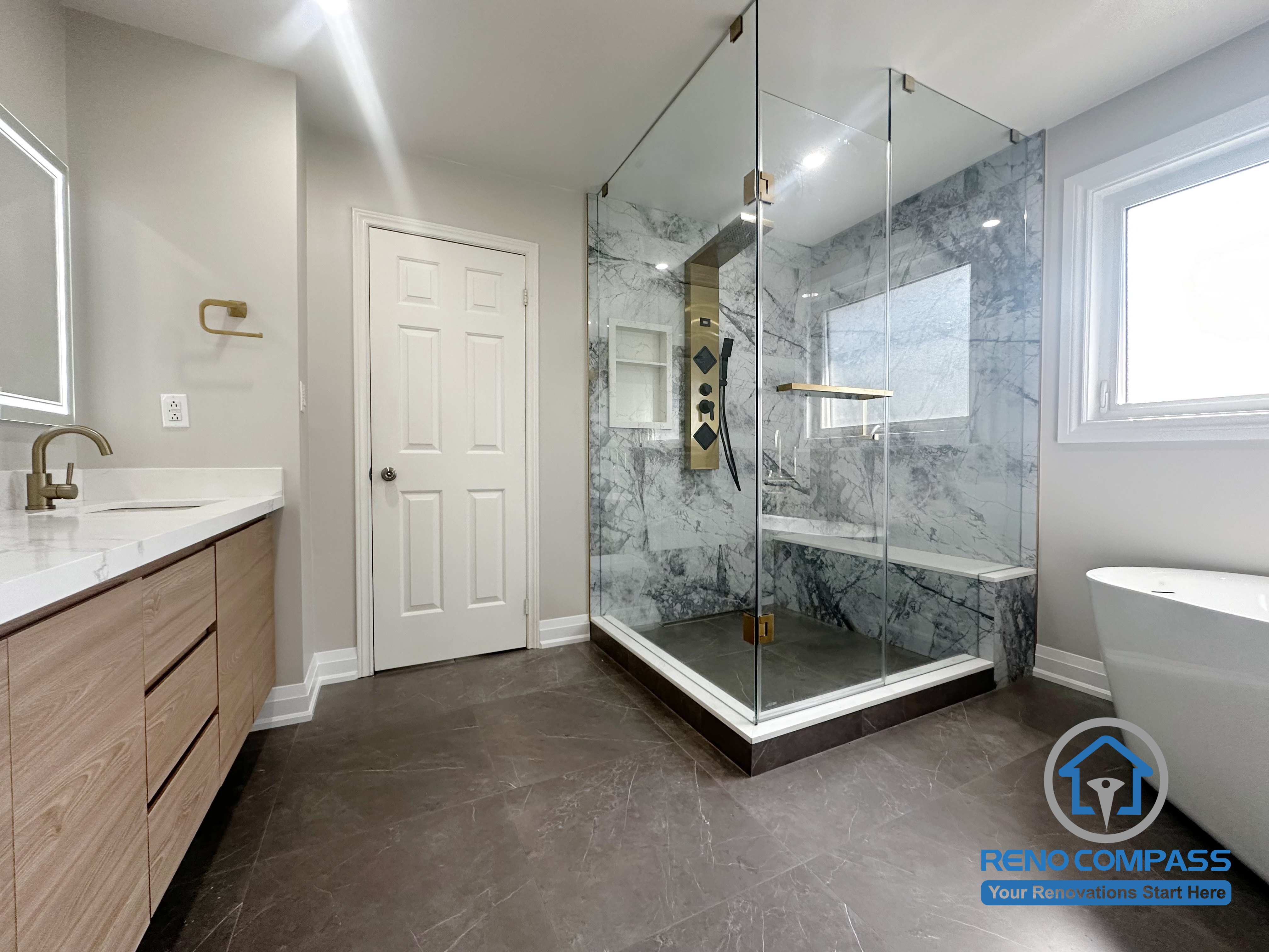 This Oakville bathroom renovation captures the overall layout, connecting the vanity area, frameless glass shower, and freestanding tub within a clear and efficient circulation plan. Consistent finishes, large-format floor tiles, and well-placed lighting help define each functional zone while maintaining visual continuity. Completed by Reno Compass, this design emphasizes everyday usability, spatial balance, and long-term performance in a modern Oakville home.