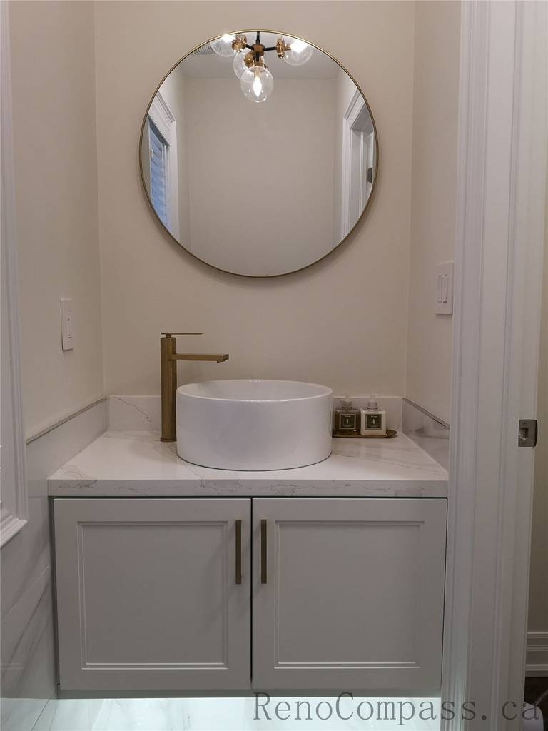 This Aurora bathroom renovation features a modern vanity with a round wall mirror, vessel sink, quartz countertop, and elegant brushed gold faucet. The clean cabinetry and soft lighting create a bright and refined space with a timeless contemporary look. Completed by a professional Toronto renovation company focused on quality finishes, functional design, and detailed craftsmanship.