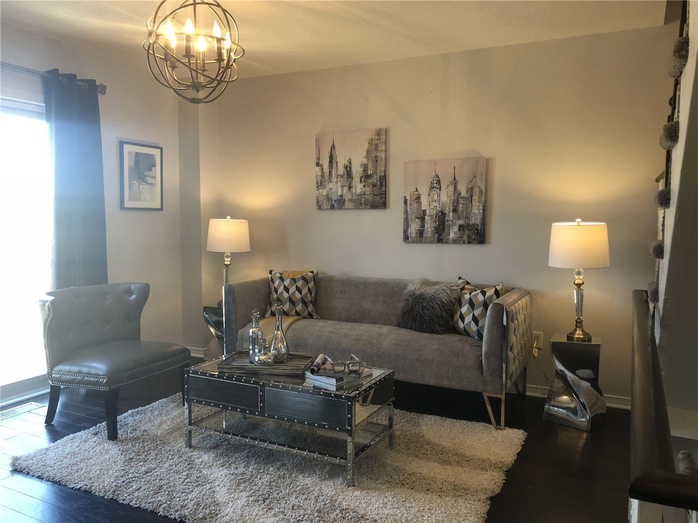 This Toronto interior design pre-sale staging highlights a stylish family living room with modern lighting, neutral-tone sofa, accent chair, and layered décor. The soft area rug, contemporary artwork, and coordinated furniture layout create a cozy yet upscale atmosphere that enhances space and comfort.