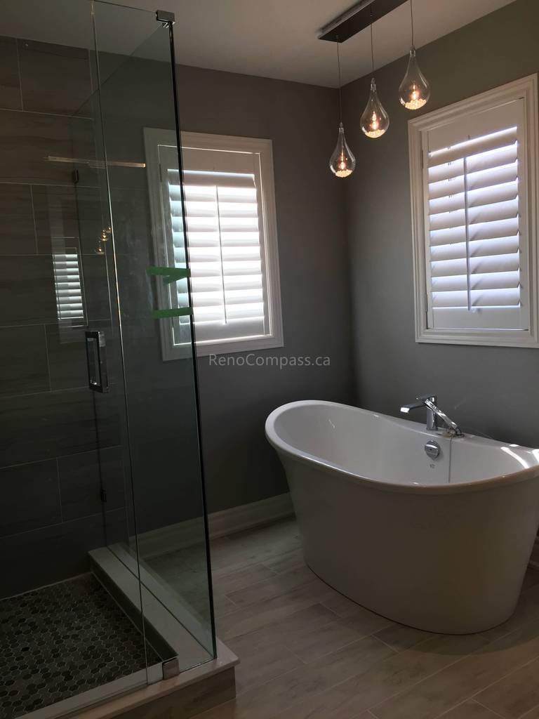 A spa-inspired bathroom interior renovation in Toronto featuring a glass-enclosed walk-in shower, freestanding bathtub, modern pendant lighting, and neutral-toned finishes. The space balances functionality and relaxation, showcasing refined Toronto interior renovation and interior design craftsmanship.