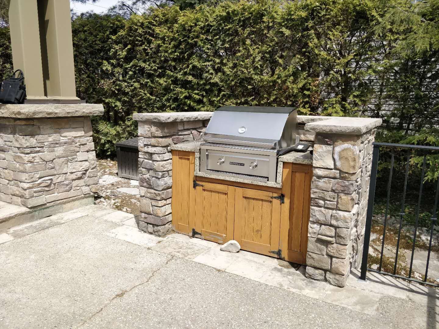 Custom outdoor BBQ station in Oakville featuring natural stone pillars, built-in grill, and wood cabinet storage. Designed for durability, functionality, and elegant backyard entertaining.
