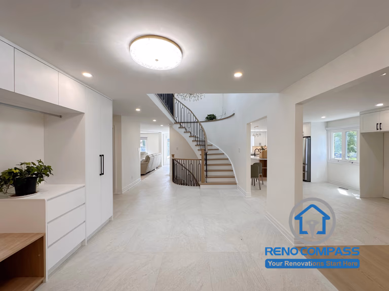 A grand foyer featuring a custom curved staircase, double-height ceiling, built-in mudroom storage, and an open-concept layout connecting the living room, kitchen, and dining area. Completed during a luxury whole home renovation in Markham, Ontario, this elegant entrance showcases premium craftsmanship, custom millwork, and timeless interior design by Reno Compass.