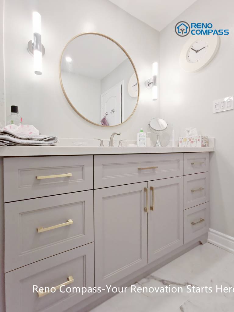 This Mississauga bathroom renovation features a custom vanity with soft grey cabinetry, brushed gold hardware, and a clean quartz countertop. A round framed mirror paired with vertical wall sconces provides balanced lighting for daily use while enhancing the overall elegance of the space. Thoughtful storage design and refined finishes reflect the attention to detail and craftsmanship expected from a professional Toronto renovation company.