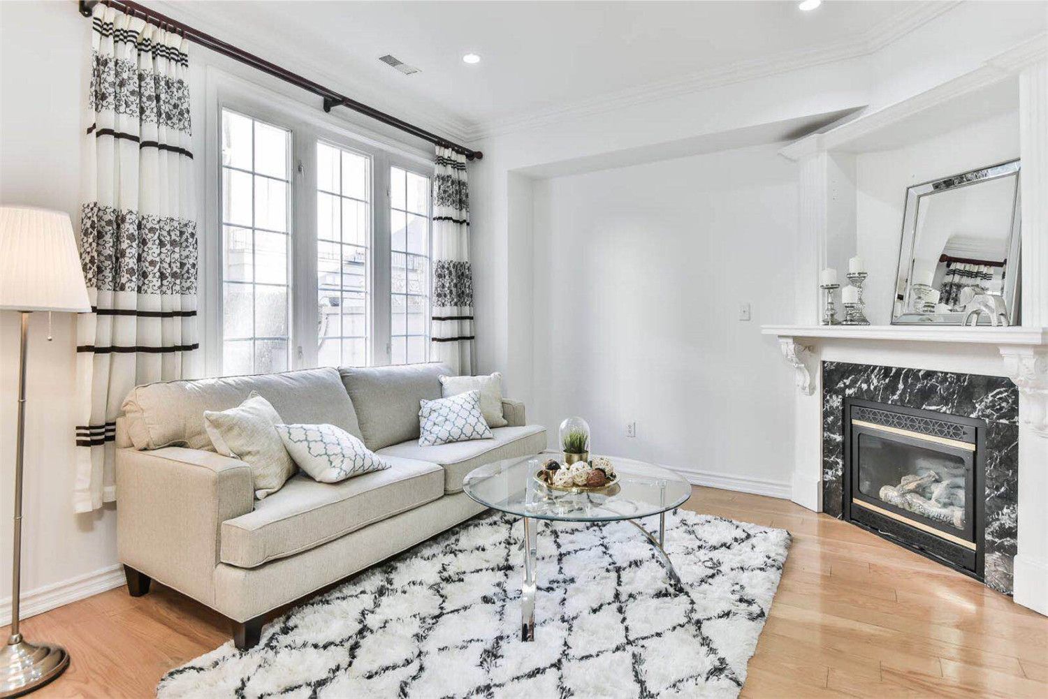 This project features a professionally staged living room in a Toronto townhouse prepared for sale. The space highlights a bright and welcoming atmosphere with a light-colored sofa, patterned curtains, soft textured rug, and a modern glass coffee table. Natural light from large windows enhances the clean white interior, while the fireplace adds warmth and elegance to the room. Professional home staging helps present the property at its best, allowing potential buyers to better visualize the space and increasing overall market appeal.
