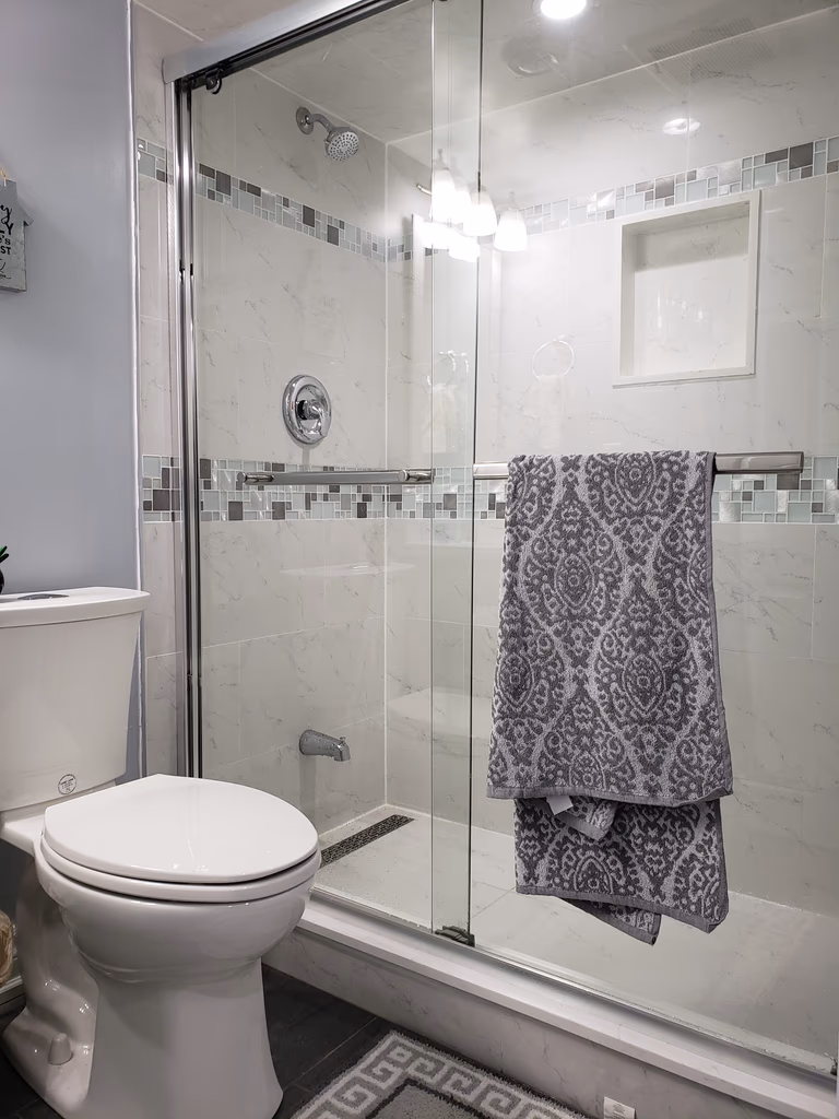 This basement bathroom renovation in Newmarket, Toronto features a clean and modern design with a glass-enclosed shower, full-height wall tiles, and upgraded plumbing fixtures. The shower area includes a built-in niche and decorative accent tile band, combining functionality with contemporary style. Neutral tones and bright lighting enhance the sense of space, making the bathroom feel fresh and inviting despite the basement setting. Durable floor tiles and moisture-resistant materials ensure long-term performance and easy maintenance. Completed by a professional Toronto renovation company, this basement bathroom upgrade focuses on practicality, comfort, and modern interior aesthetics.