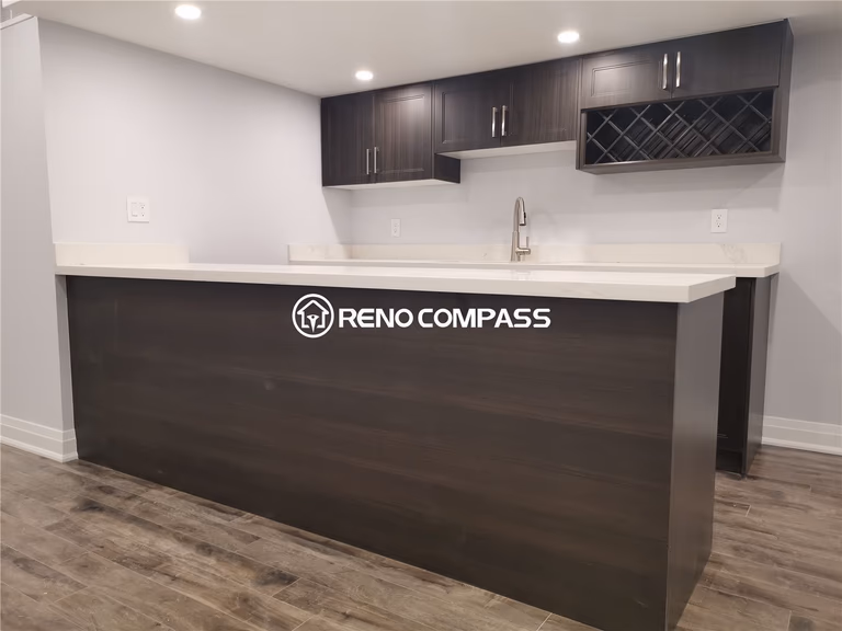 This Markham basement renovation features a custom-built bar counter and modern kitchenette designed for entertaining and everyday convenience. The extended quartz countertop provides generous seating and preparation space, while dark wood cabinetry and a built-in wine rack add both functionality and style. Waterproof vinyl flooring and recessed pot lights enhance the overall modern basement atmosphere. Completed by a professional Toronto renovation company, this project highlights quality craftsmanship, custom millwork, and practical basement remodeling solutions tailored for contemporary homes across the Greater Toronto Area.