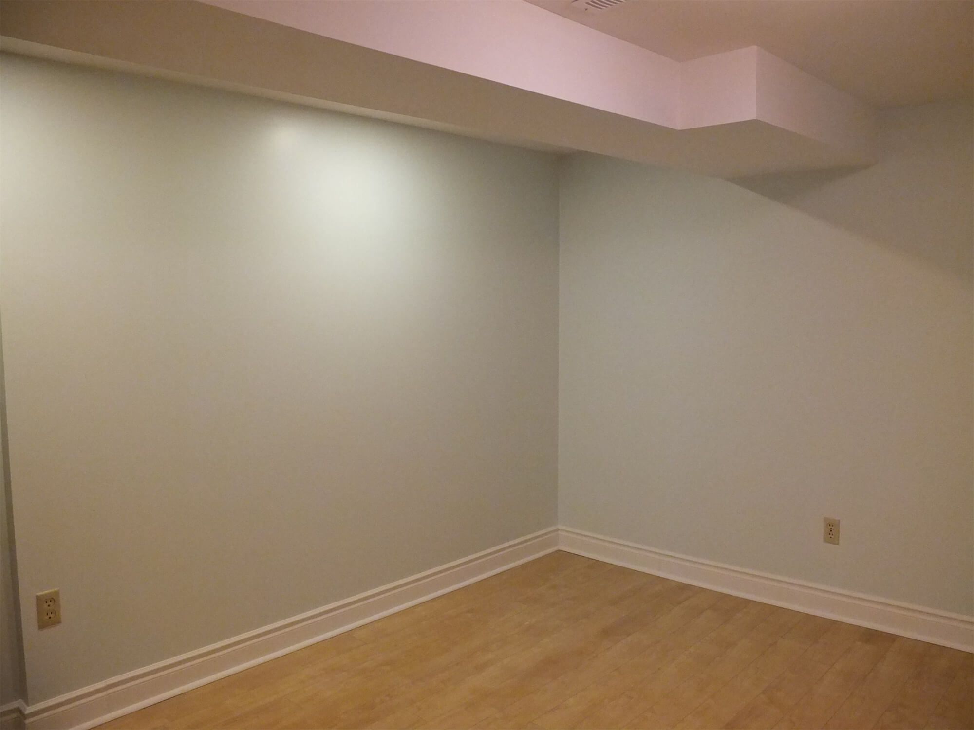 This Oshawa basement renovation showcases a clean and newly finished lower-level living space with smooth painted walls, updated baseboards, and durable wood-style flooring. The structured ceiling bulkhead is seamlessly integrated into the design, maintaining a tidy and cohesive look. Neutral tones create a bright and adaptable environment, making the space ideal for a home office, recreation area, or guest room. Completed by a professional Toronto Renovation Company, this project reflects precise finishing work and practical basement transformation designed for everyday functionality.