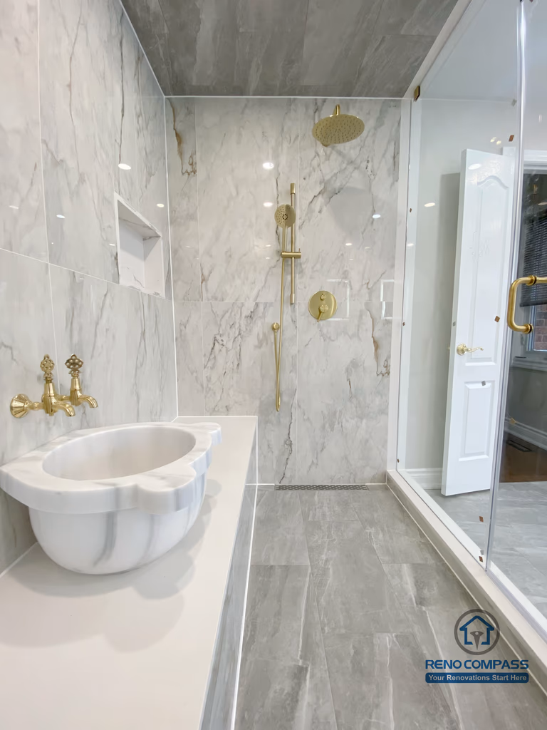 This Richmond Hill bathroom renovation showcases a bright and elegant design featuring a frameless glass shower enclosure, built-in bathtub, marble-style wall tiles, and gold-finish fixtures. The custom white vanity with integrated lighting mirror and large-format floor tiles enhance both functionality and visual openness. This project reflects high-quality craftsmanship and thoughtful layout planning for a modern bathroom renovation in Richmond Hill.