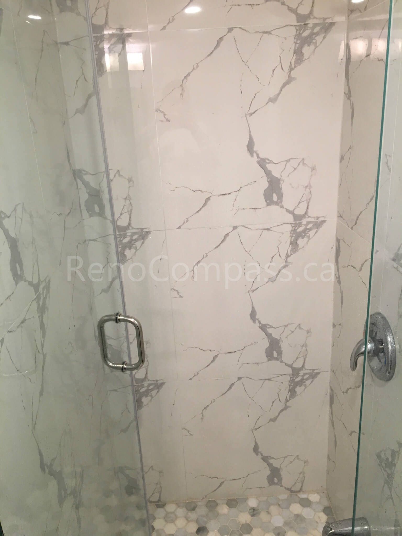 A luxurious frameless glass shower enclosure featuring elegant marble-pattern wall tiles and pebble-style flooring. This Mississauga bathroom renovation by RenoCompass delivers a spa-like experience with high-end materials and craftsmanship.