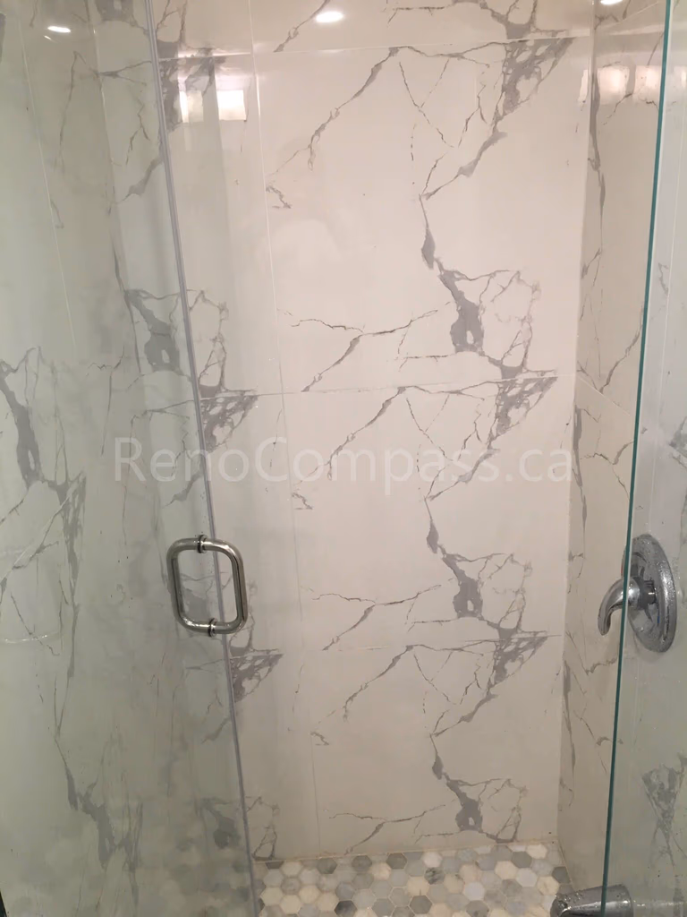 A luxurious frameless glass shower enclosure featuring elegant marble-pattern wall tiles and pebble-style flooring. This Mississauga bathroom renovation by RenoCompass delivers a spa-like experience with high-end materials and craftsmanship.