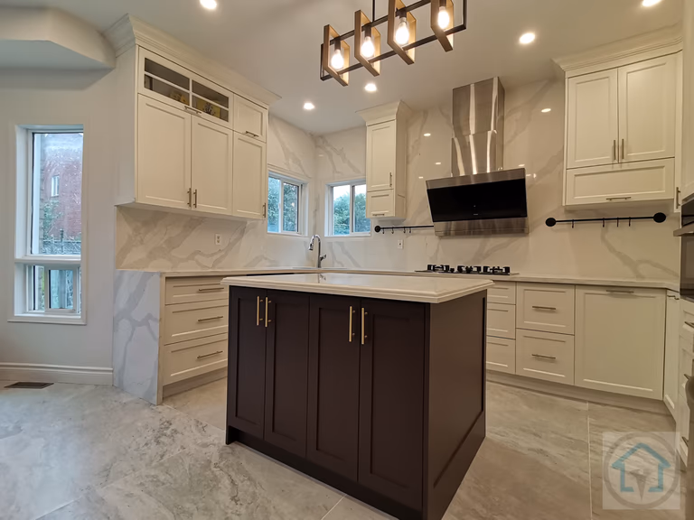 This bright white kitchen renovation showcases a clean, symmetrical layout centered around a statement dark-toned island. Full-height custom cabinetry, marble-look backsplash, and large-format floor tiles create a cohesive and upscale visual flow while enhancing light reflection throughout the space. The central island anchors the kitchen with added storage and prep space, making it ideal for both daily use and entertaining. Stainless steel appliances, integrated lighting, and a modern range hood complete the design with a balance of functionality and elegance. Completed by an experienced Toronto renovation company, this kitchen renovation highlights thoughtful planning, refined material selection, and long-term livability for modern family homes.