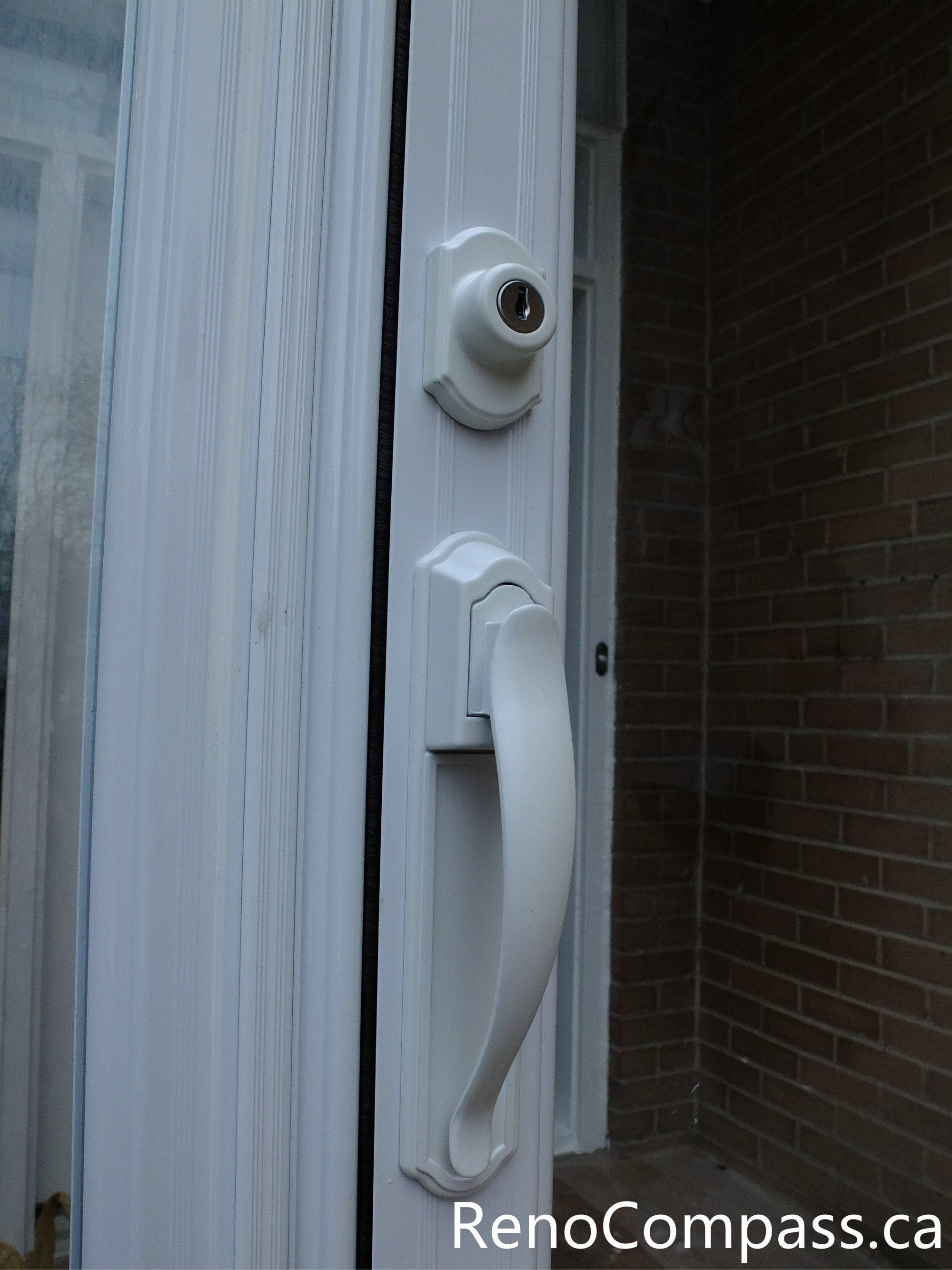 This close-up image shows the handle and lock detail of a newly installed glass storm door at a North York residential entrance. The durable white handle and secure locking system provide convenient access while improving safety and weather protection. The storm door enclosure helps shield the main entrance from wind, snow, and rain, while the clear glass panels allow natural light to enter the foyer. Installed by a professional Toronto renovation team, this entrance upgrade enhances both security and the overall appearance of the home.