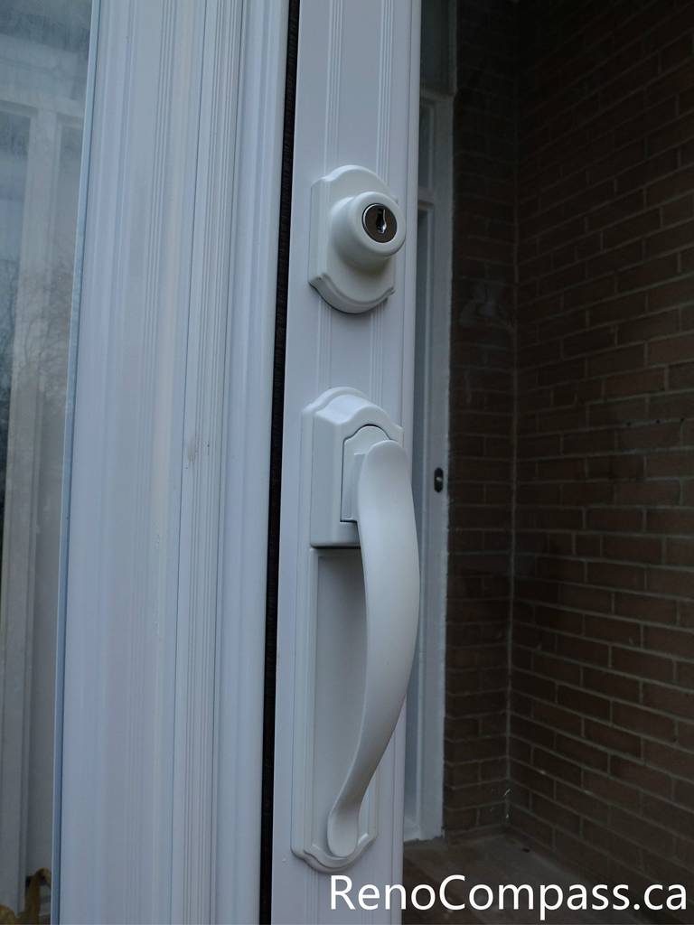 This close-up image shows the handle and lock detail of a newly installed glass storm door at a North York residential entrance. The durable white handle and secure locking system provide convenient access while improving safety and weather protection. The storm door enclosure helps shield the main entrance from wind, snow, and rain, while the clear glass panels allow natural light to enter the foyer. Installed by a professional Toronto renovation team, this entrance upgrade enhances both security and the overall appearance of the home.
