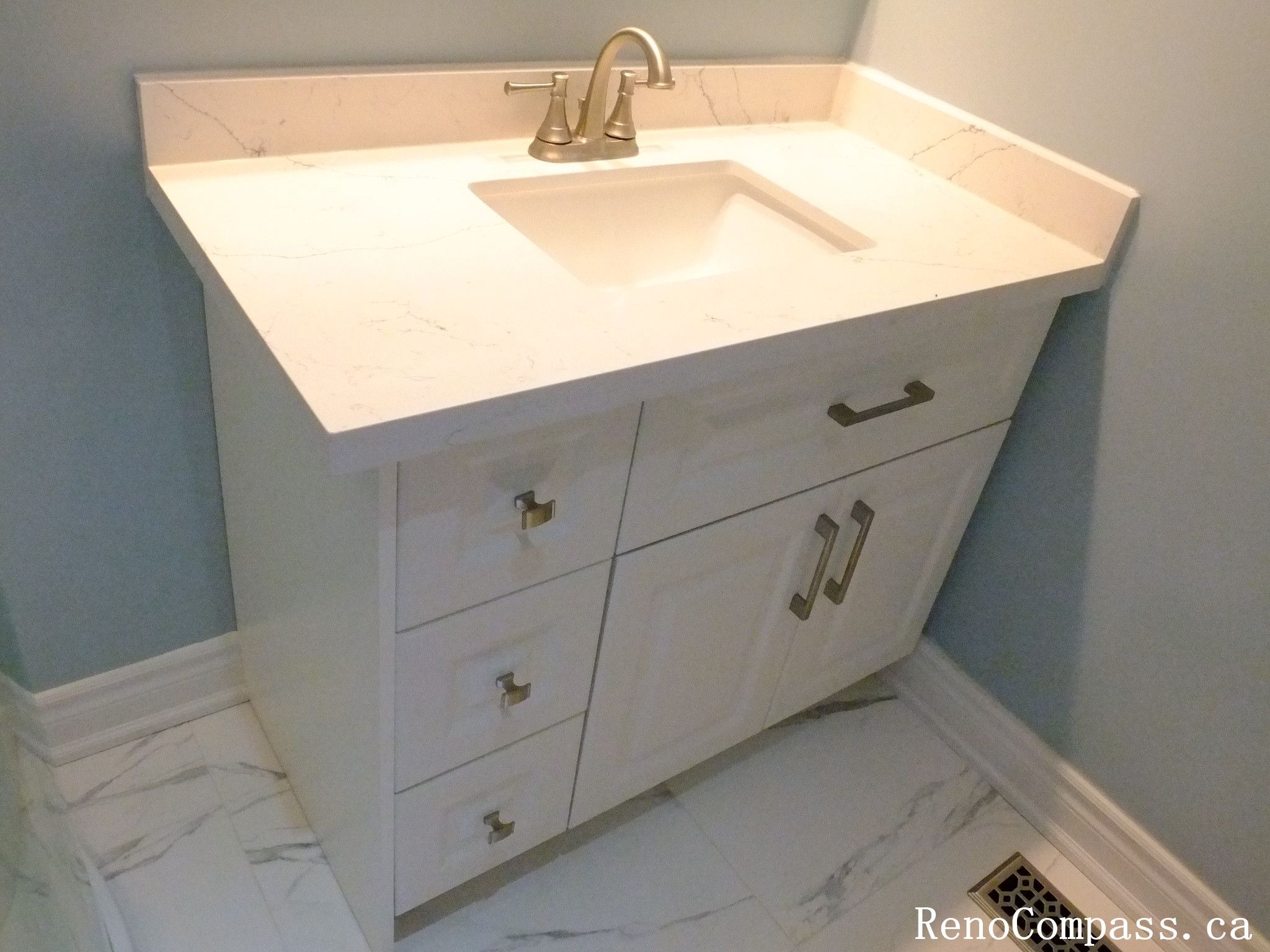 This Richmond Hill bathroom renovation highlights a custom vanity installation featuring a quartz countertop, integrated sink, and modern cabinetry. The clean lines and bright finishes enhance both functionality and style, while the marble-look tile flooring adds a refined touch. Completed by a Toronto renovation company, this detail showcases high-quality craftsmanship in bathroom design.