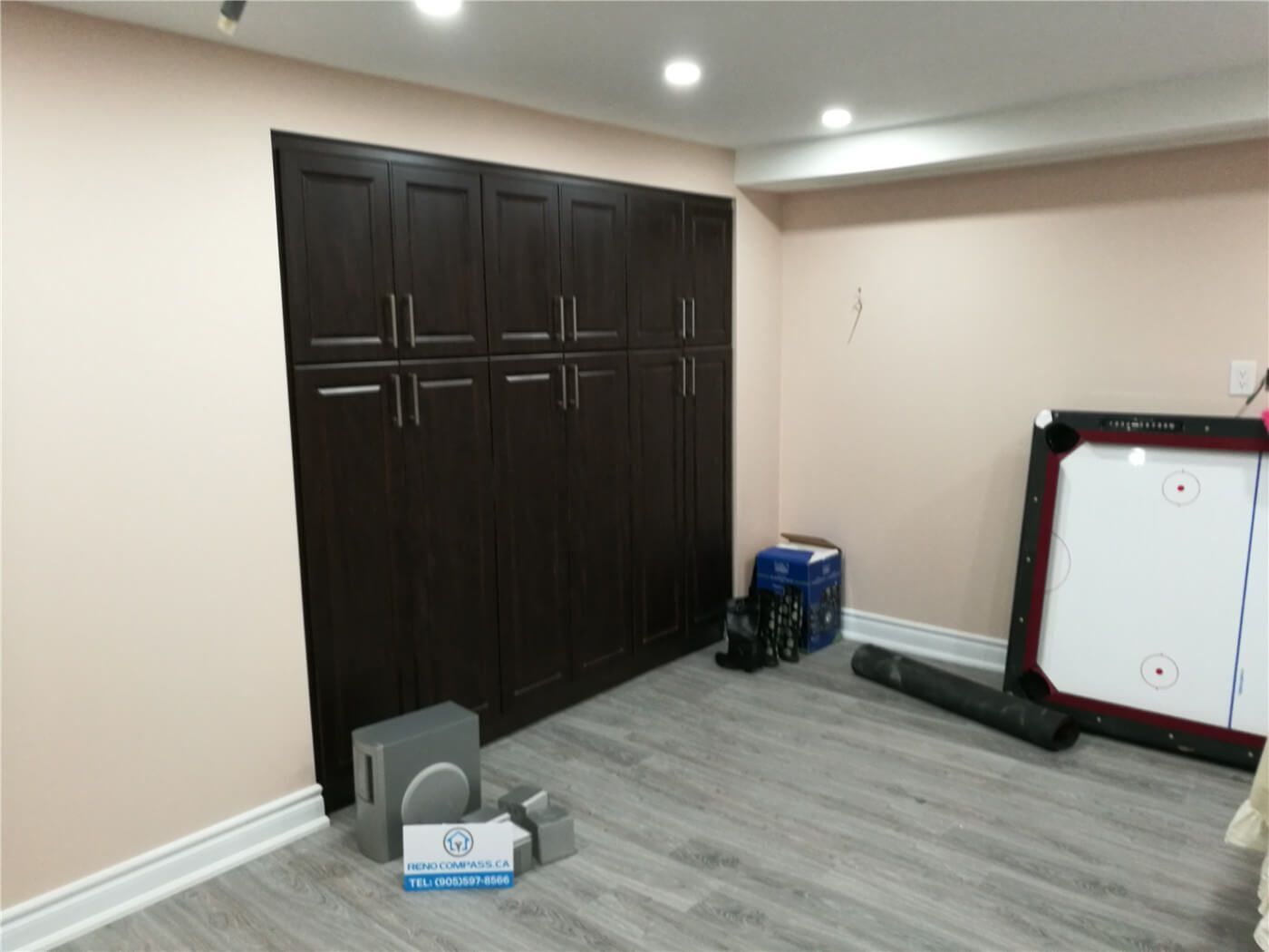 This image features custom built-in storage cabinets completed as part of a Newmarket interior renovation project. The floor-to-ceiling dark wood cabinetry provides ample storage while maintaining a clean, modern appearance. Integrated handles and recessed ceiling lighting enhance both functionality and visual balance within the space. Completed by a professional Toronto renovation company, this custom cabinetry solution improves organization, usability, and overall interior efficiency.