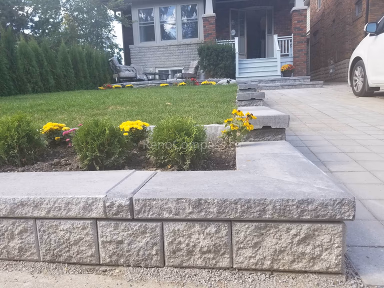 This Toronto front yard landscaping renovation highlights a structured and low-maintenance outdoor upgrade featuring a newly installed raised stone retaining wall, fresh green sod, and neatly arranged seasonal flower beds. Privacy cedar hedges line the property to create a clean and elegant backdrop, while the elevated lawn design improves drainage and visual balance. Completed by a professional Toronto landscaping renovation team, this project enhances curb appeal and creates a polished, welcoming entrance for the home.