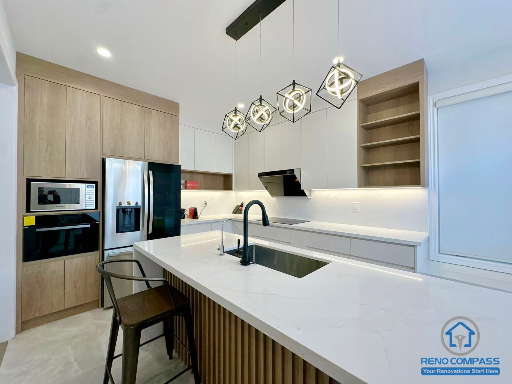 This Stouffville kitchen renovation highlights a custom island with an integrated sink, quartz countertop, and vertical wood panel detailing. Contemporary pendant lighting and a mix of wood and white cabinetry create a balanced, modern aesthetic while maintaining functionality. Completed by a trusted Toronto renovation company, Reno Compass Inc., this project reflects thoughtful kitchen design and quality interior renovation workmanship.