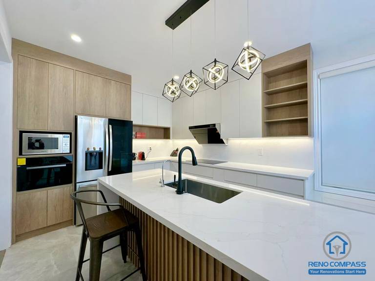 This Stouffville kitchen renovation highlights a custom island with an integrated sink, quartz countertop, and vertical wood panel detailing. Contemporary pendant lighting and a mix of wood and white cabinetry create a balanced, modern aesthetic while maintaining functionality. Completed by a trusted Toronto renovation company, Reno Compass Inc., this project reflects thoughtful kitchen design and quality interior renovation workmanship.