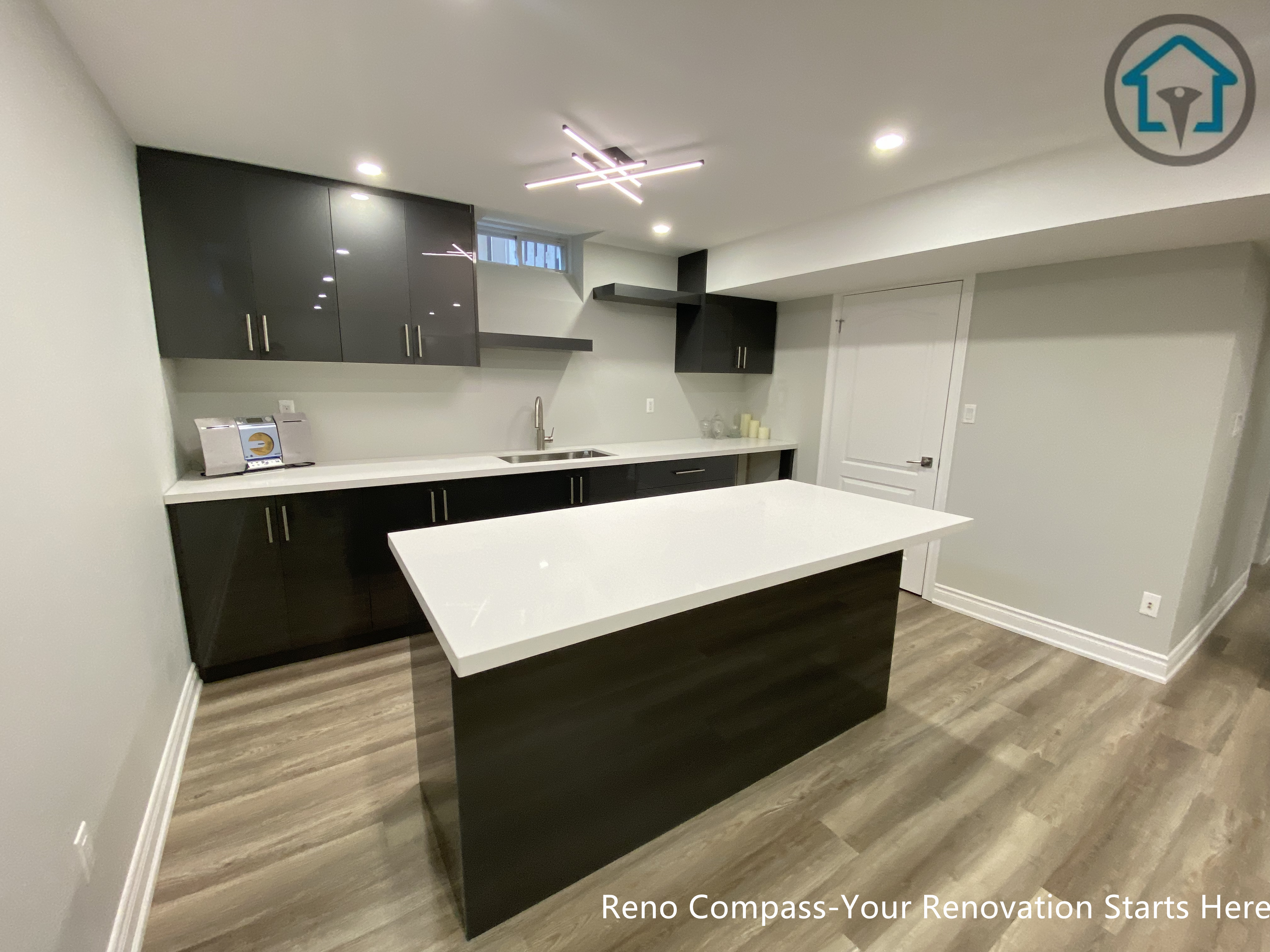 A modern basement kitchen renovation in Markham featuring a large quartz island, custom dark cabinetry, integrated lighting, and durable flooring, creating a functional and stylish lower-level living space.