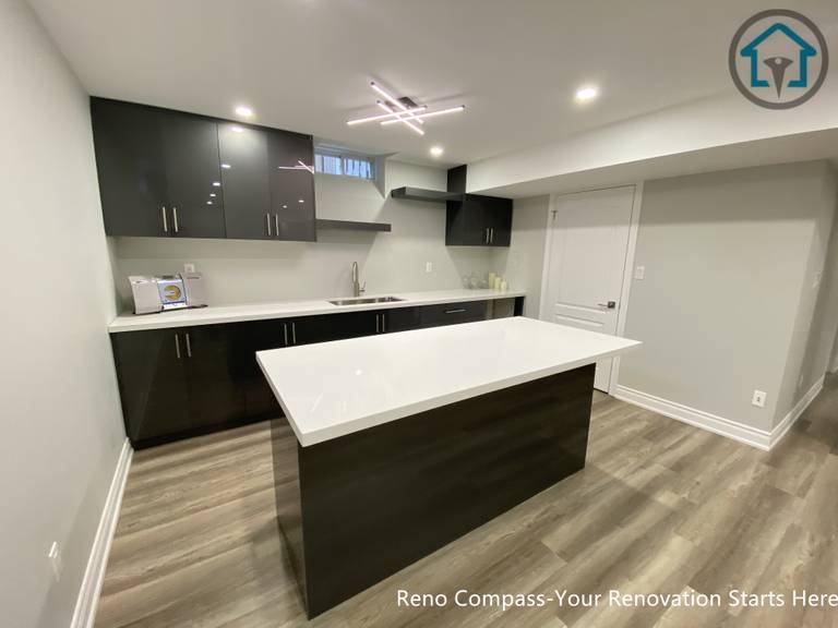 A modern basement kitchen renovation in Markham featuring a large quartz island, custom dark cabinetry, integrated lighting, and durable flooring, creating a functional and stylish lower-level living space.