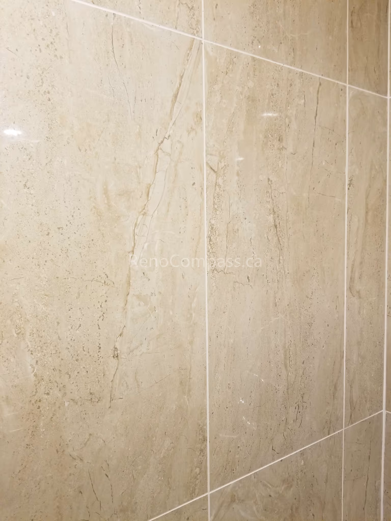 This Vaughan basement bathroom renovation highlights premium beige marble-look wall tile installation, creating a clean, elegant, and moisture-resistant shower environment. The large-format tiles and precise grout lines deliver a seamless modern finish while improving durability and easy maintenance. Professionally completed by Reno Compass Inc., this detailed tile work enhances both the visual appeal and functionality of the upgraded basement bathroom space.