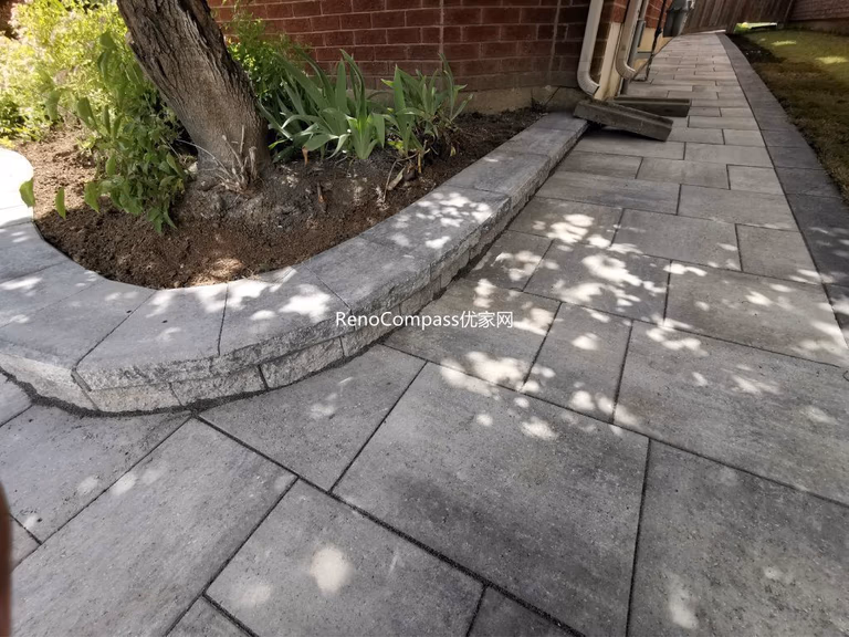 Beautifully finished side walkway interlocking project in Richmond Hill. The light gray stone pavers are neatly aligned against the house, featuring a raised garden border for a clean and modern look. Installed by Reno Compass for improved drainage, durability, and curb appeal.
