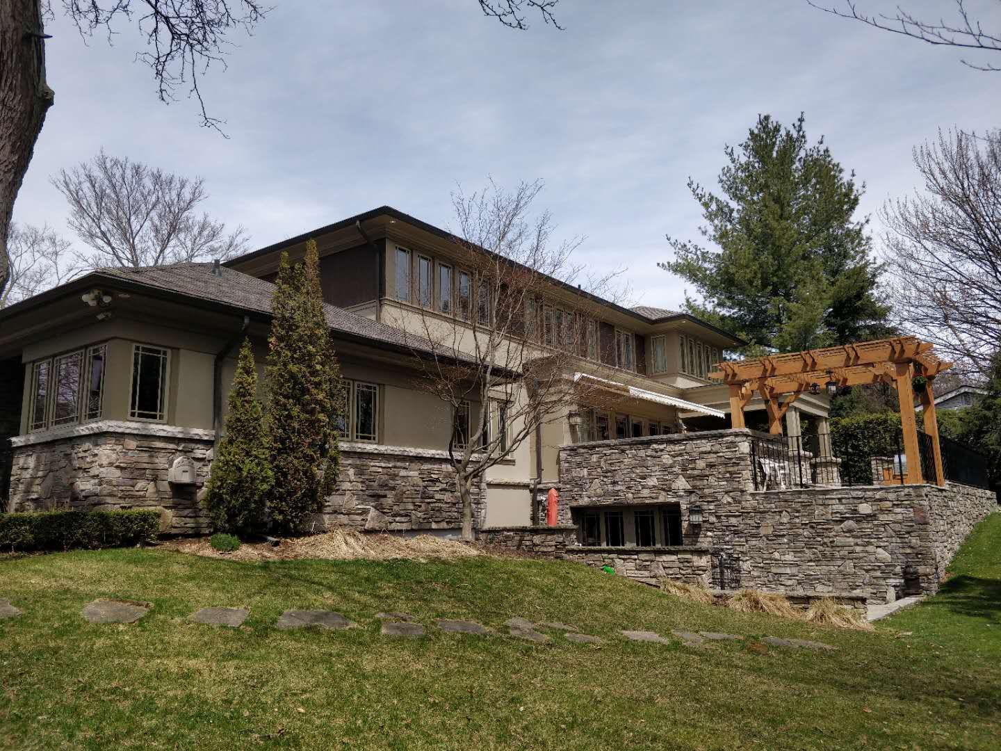 Professional Oakville landscaping project featuring natural stone retaining walls, a custom wooden pergola, and a well-integrated sloped lawn design. Built for durability, drainage, and elegant outdoor living space enhancement.